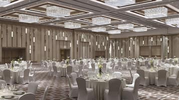 A spacious banquet hall with round tables, white chairs, and chandeliers.
