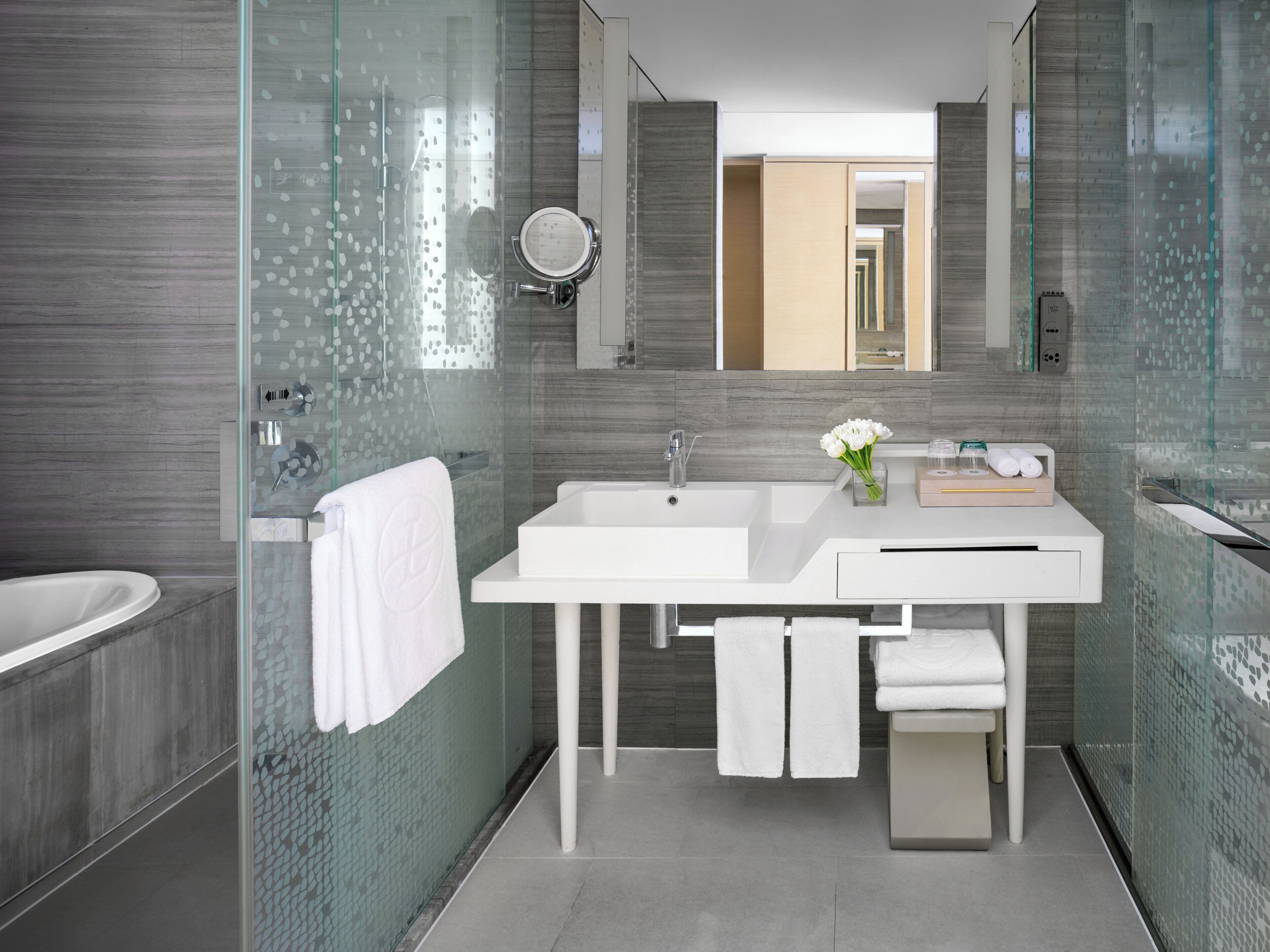 A modern bathroom with a glass-enclosed shower, a white sink, and a mirror above it.