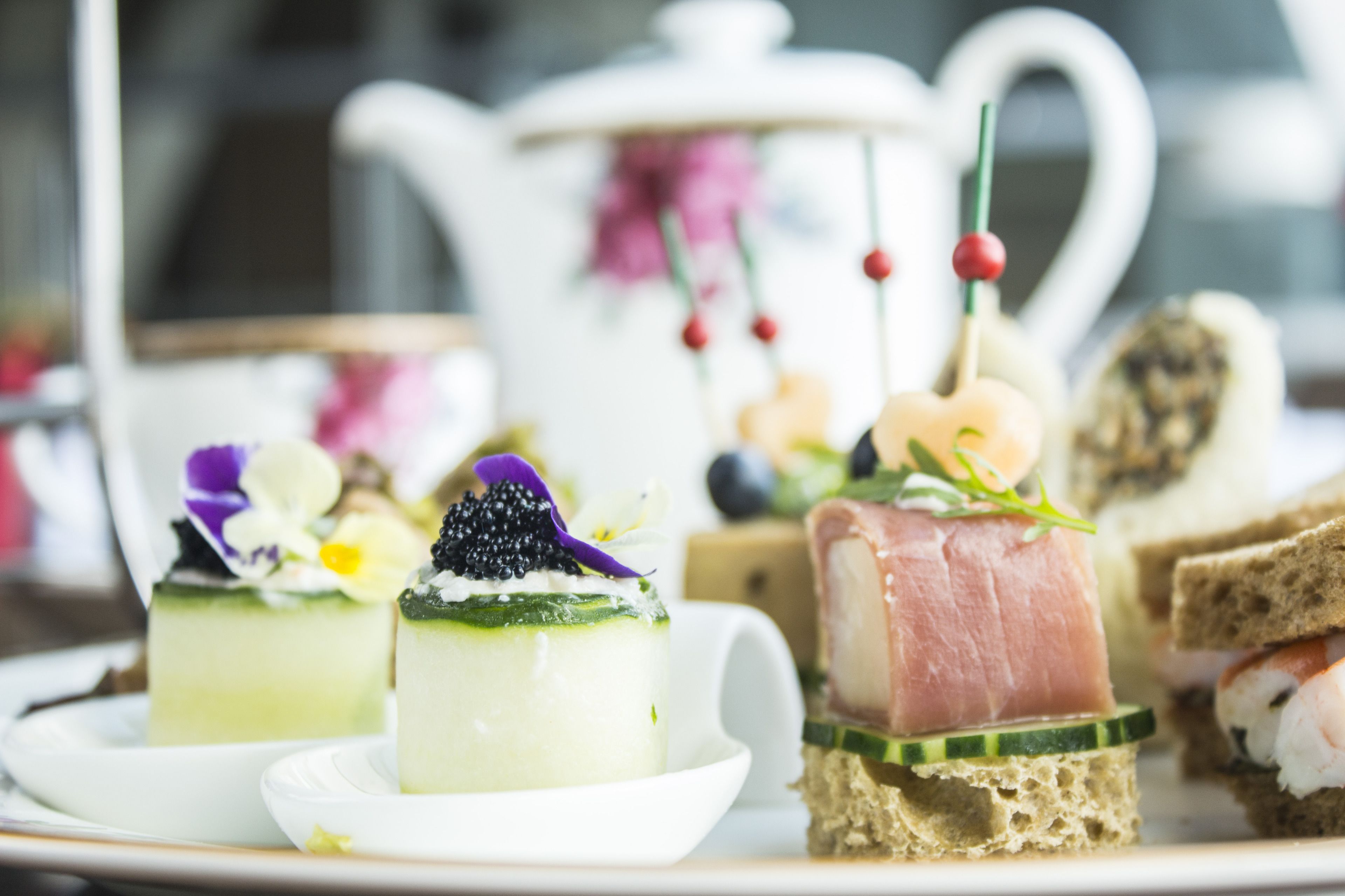 A variety of small, elegantly presented food items on a plate, including a piece of cake with a green topping and a slice of meat on bread.
