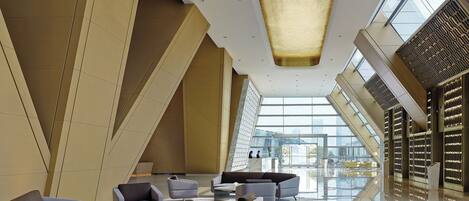 A modern lobby with geometric walls, a central light fixture, and a view of the city through large windows.