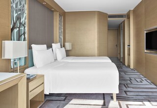 A hotel room with a large bed, two bedside tables, a desk, a TV, and a patterned carpet.