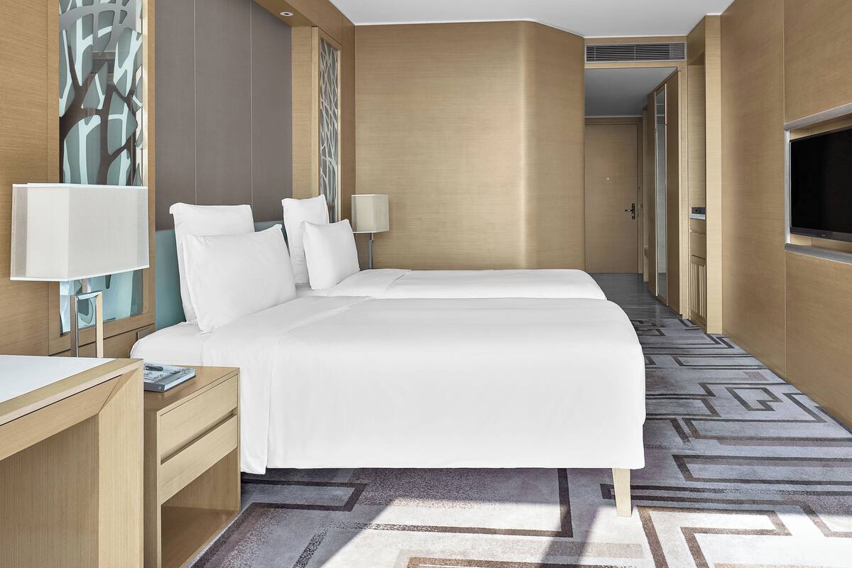 Habitación de hotel con una cama grande, dos mesitas de noche, un escritorio, un televisor y una alfombra estampada.
