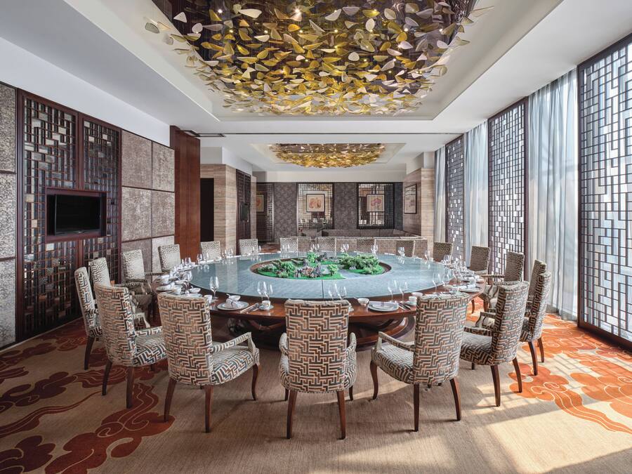 A conference room with a round table, patterned chairs, and a decorative ceiling.