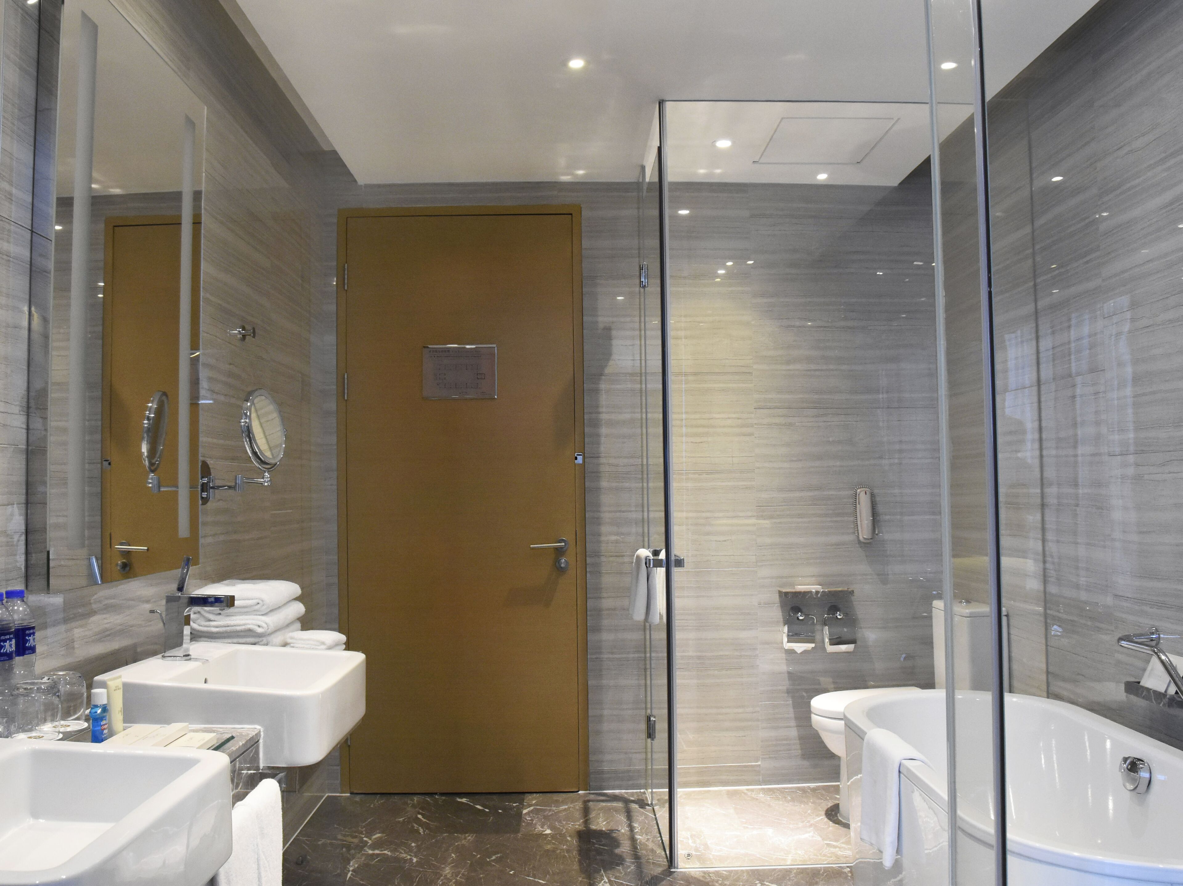 Un baño moderno con ducha envuelta en vidrio, lavamanos blanco, bañera y espejo.