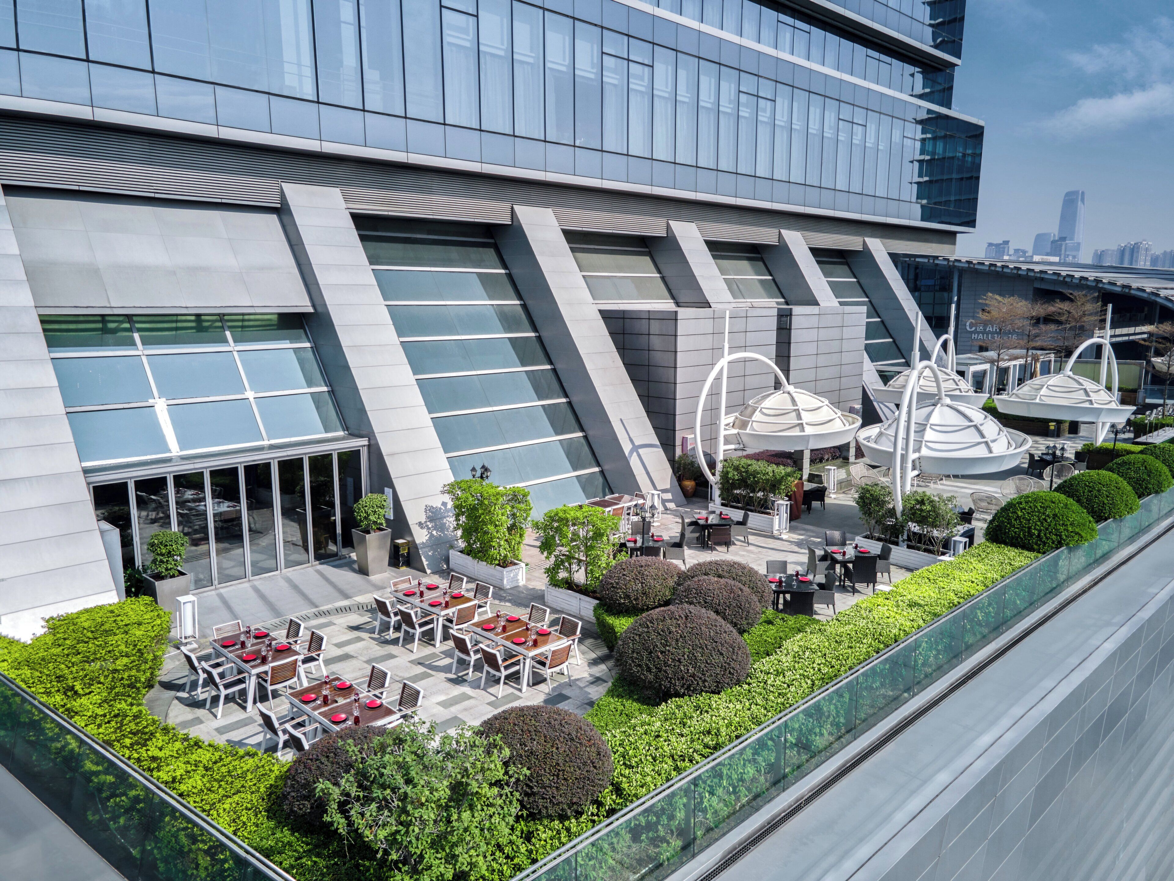 A modern building with a glass facade, outdoor seating area, and a rooftop garden.