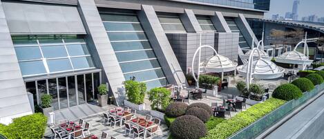 A modern building with a glass facade, outdoor seating area, and a rooftop garden.