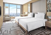 A hotel room with a large bed, a desk, a chair, and a view of the city.