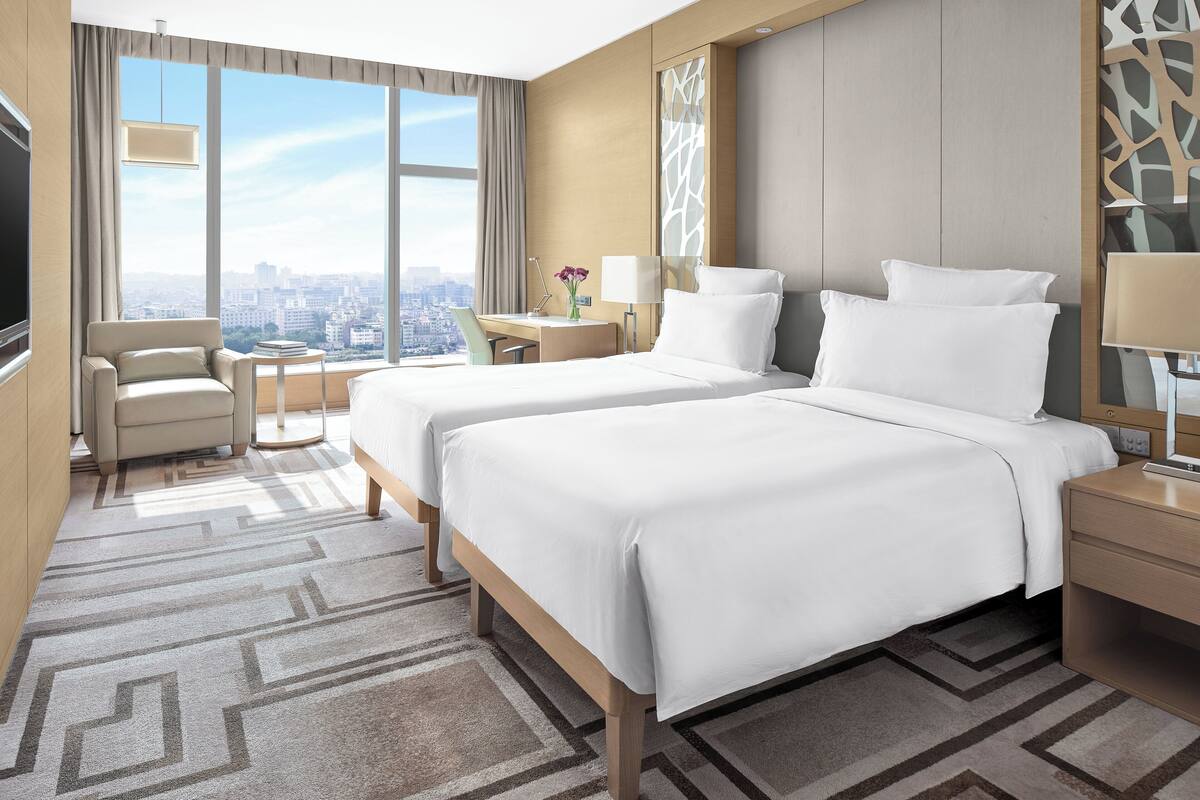 Habitación de hotel con una cama grande, un escritorio, una silla y vista a la ciudad.