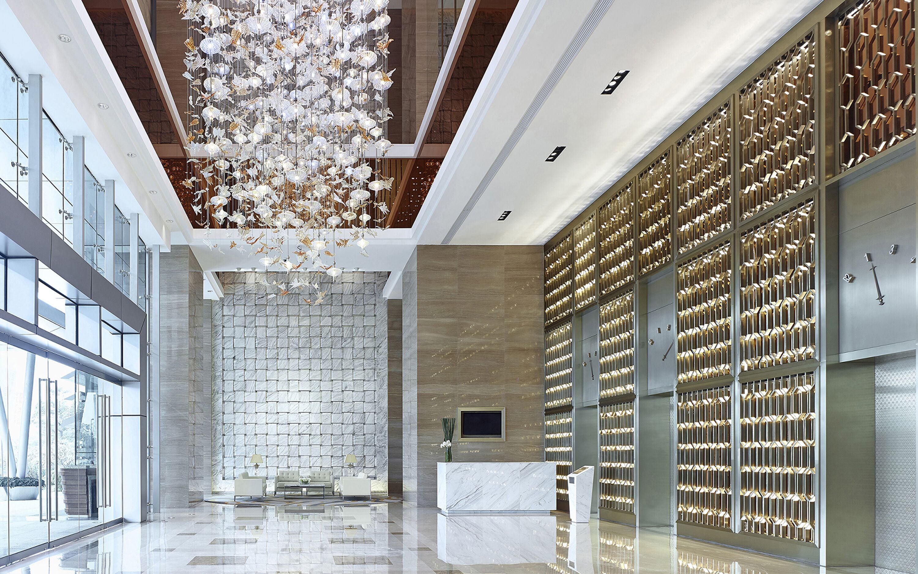 A modern lobby with a marble reception desk, a large chandelier, and a wall of lockers.
