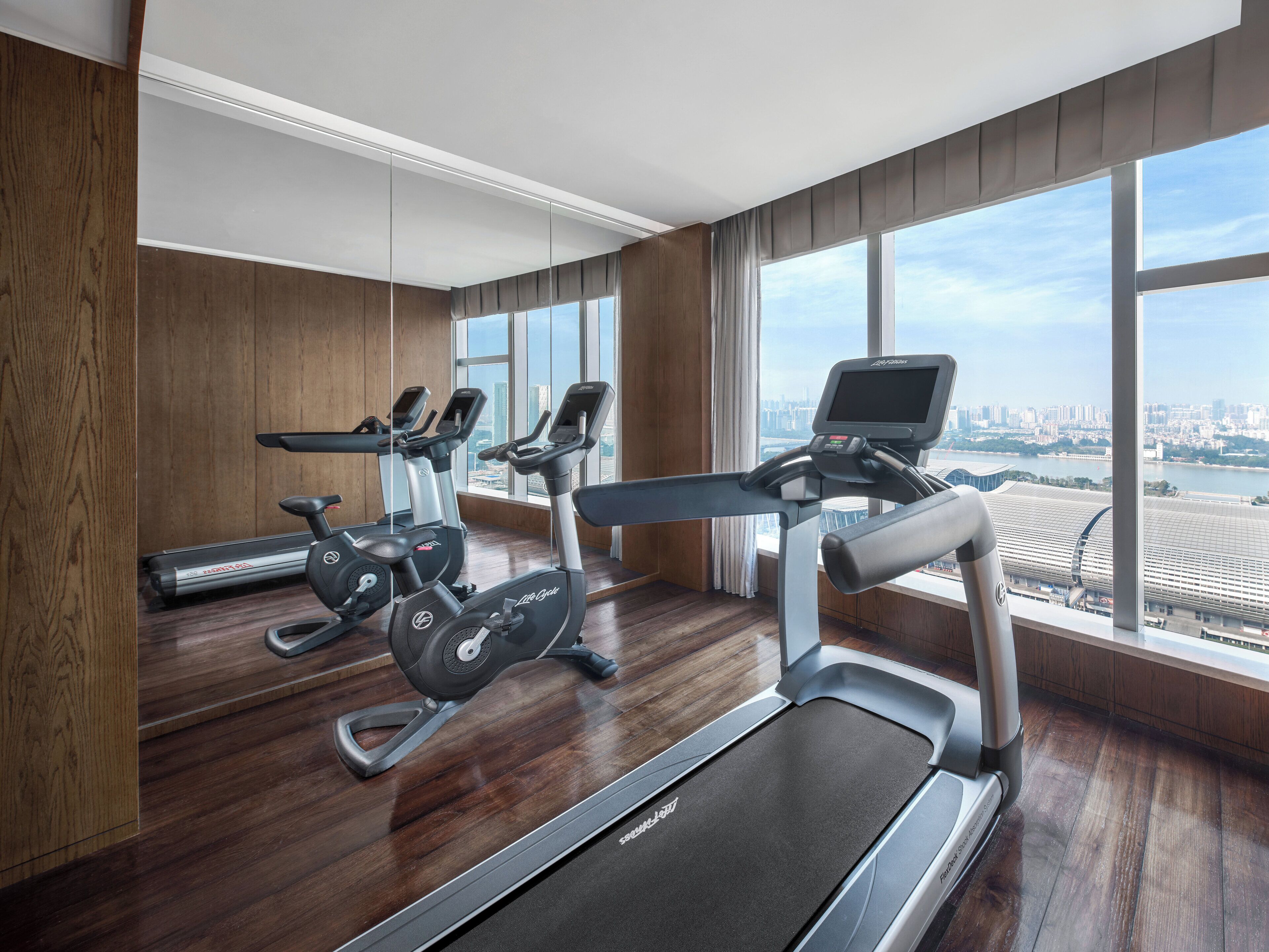 Un gimnasio moderno con cintas de correr, bicicletas estáticas y una máquina de remo. Cuenta con ventanas amplias y vistas a la ciudad.