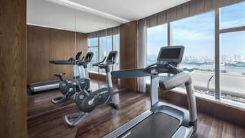 A modern gym with treadmills, stationary bikes, and a rowing machine. It features large windows with a city view.