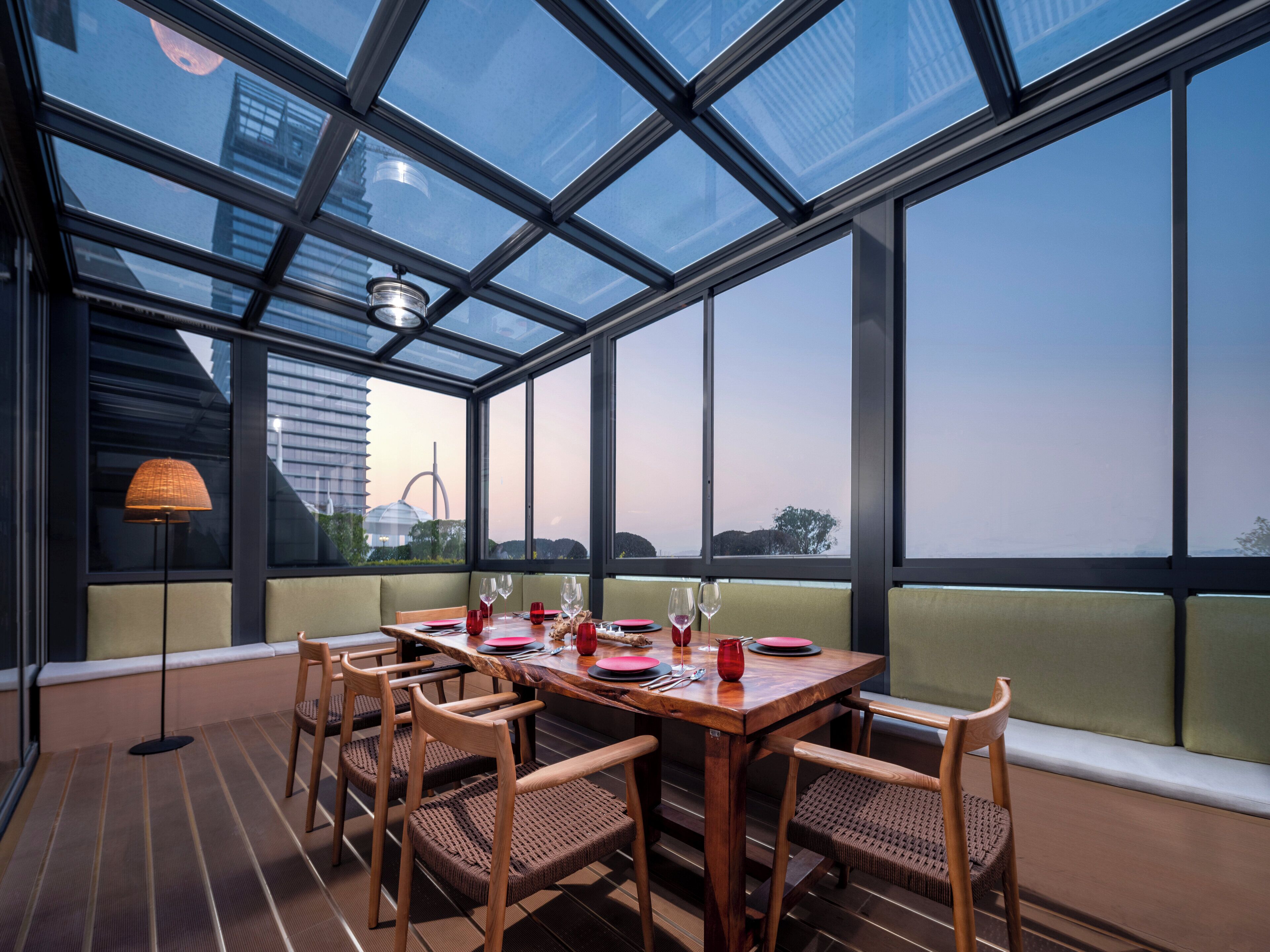 Un comedor con techo de cristal, mesa de madera y sillas.