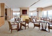 A spacious dining area with multiple tables and chairs, a bar area with a minibar, and large windows offering a city view.