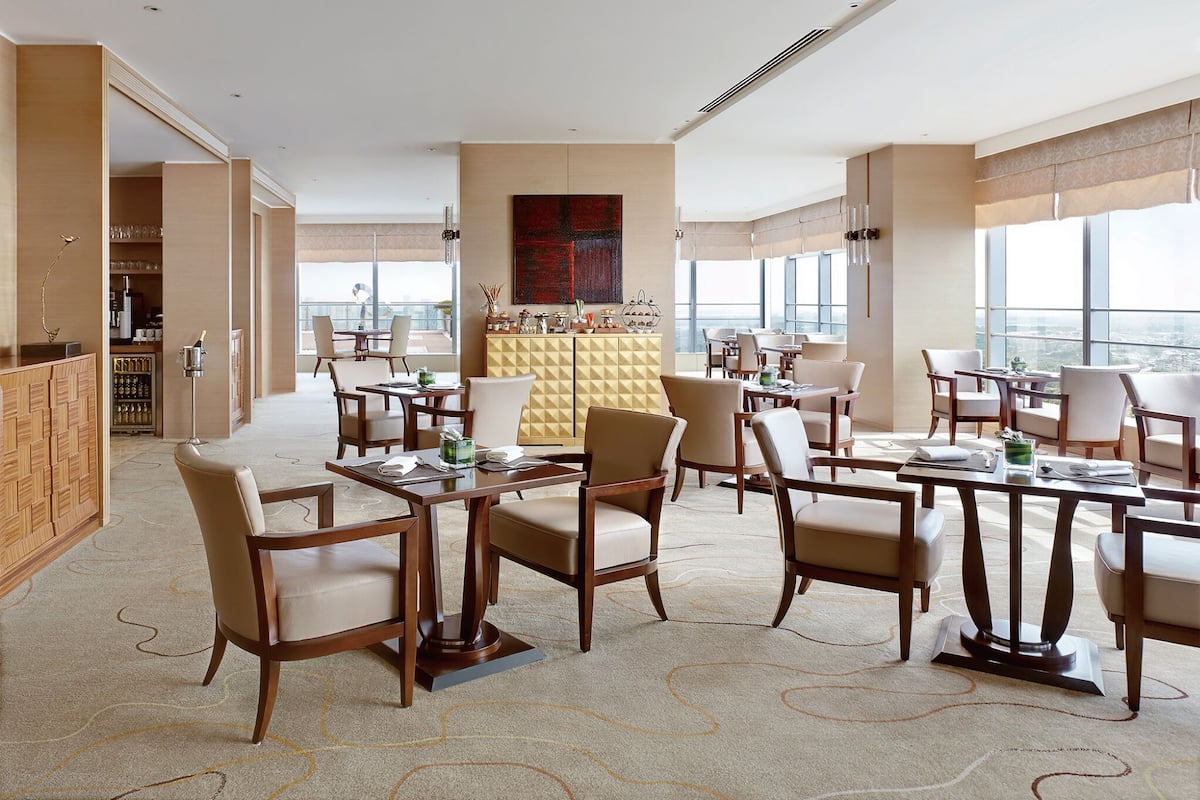 Un comedor amplio con varias mesas y sillas, una zona de bar con minibar y grandes ventanales con vistas a la ciudad.