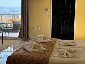 A hotel room with a bed, a window with curtains, a door, and a view of the outside.