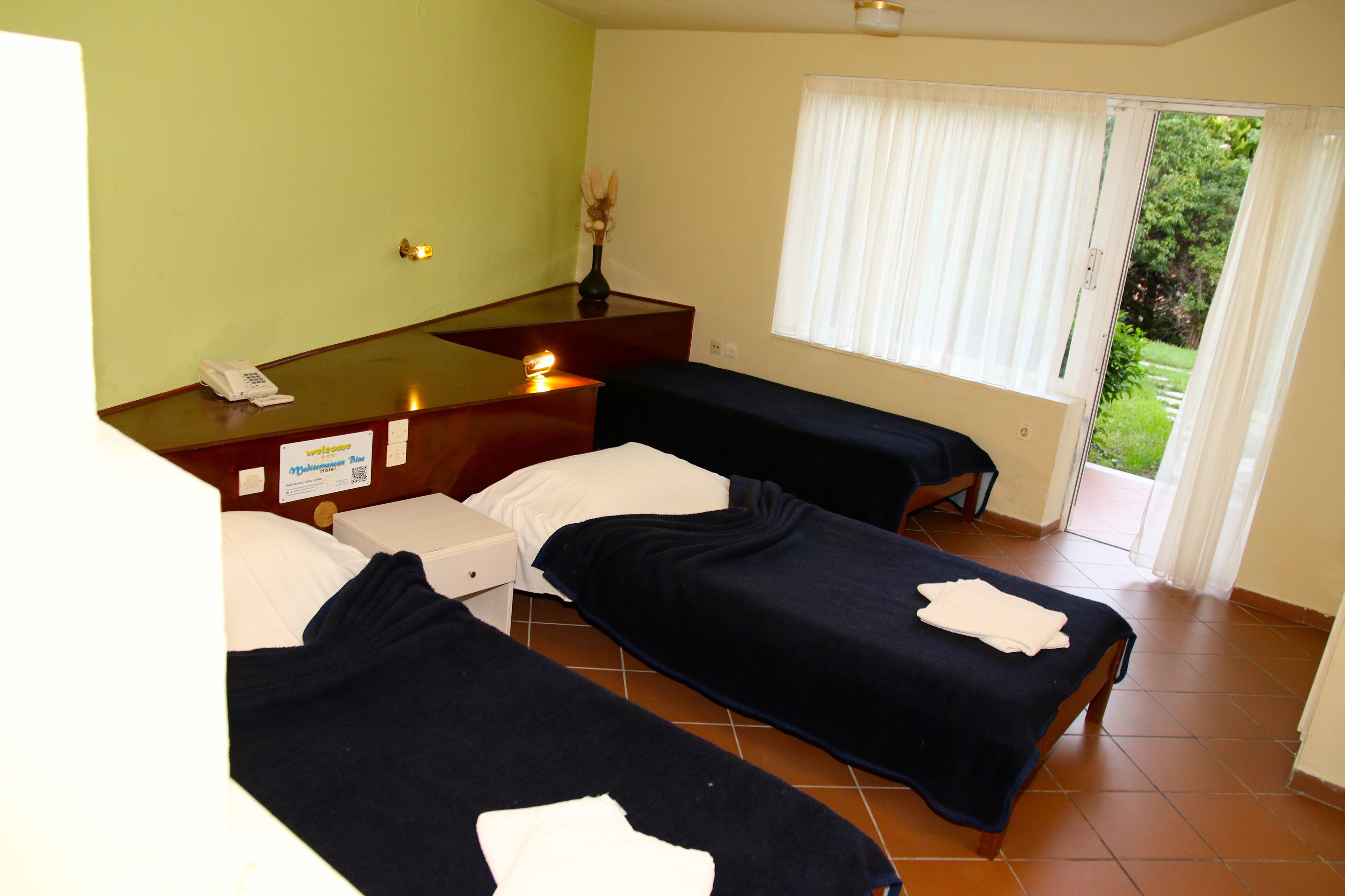 Habitación de hotel con dos camas, un escritorio con teléfono, un florero con flores y una ventana con cortinas.