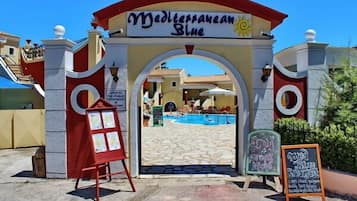 La entrada a Mediterranean Blue, con una vista despejada del área de la piscina y un cartel anunciando 'Crock Night'.