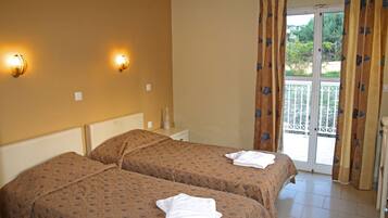 Quarto de hotel com duas camas, varanda com guarda-corrimão branco e cortinas com padrão floral.