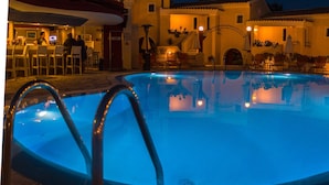 Una piscina con sillas de descanso y sombrillas, rodeada por un bar y zona de estar al aire libre.