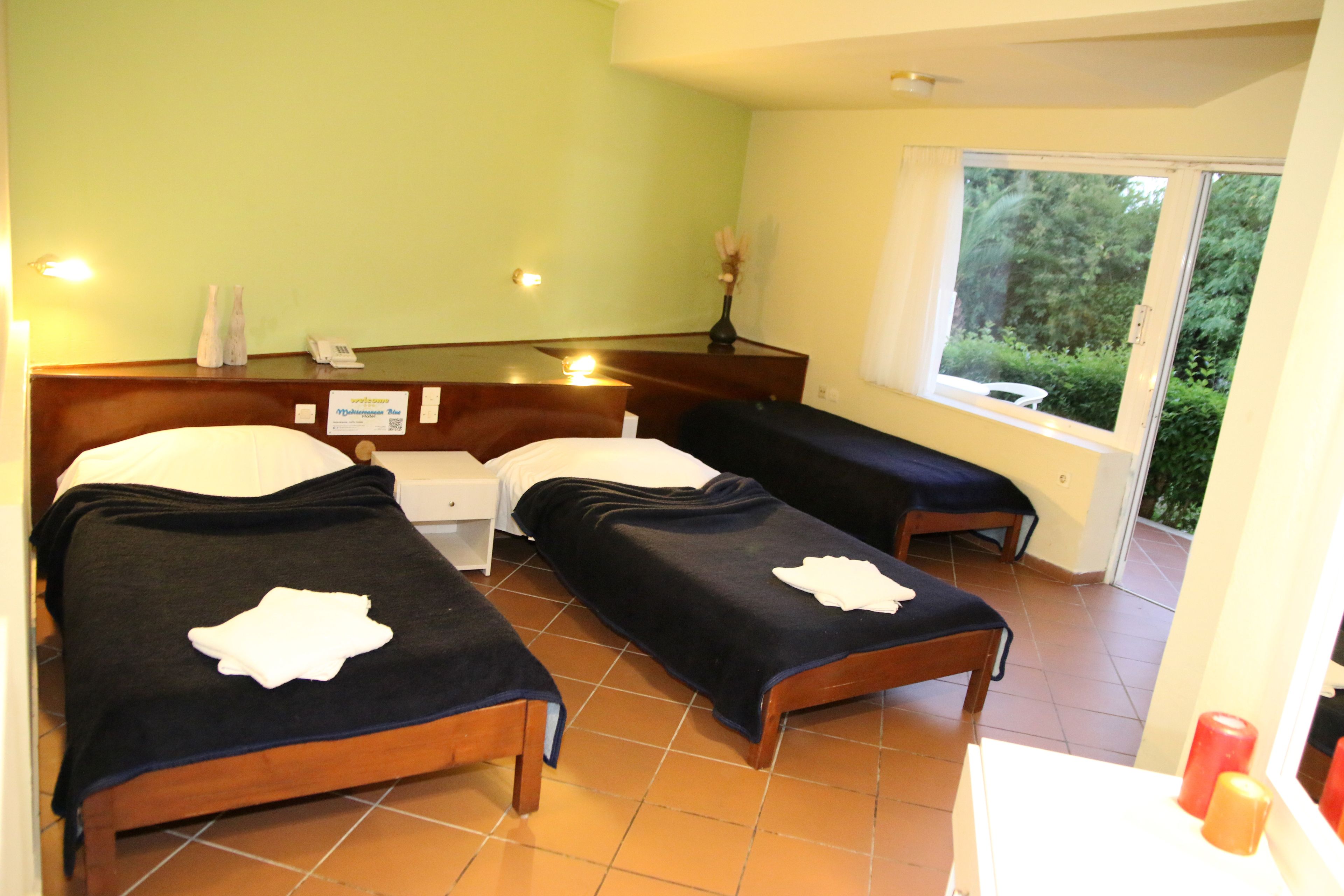 Habitación de hotel con dos camas, una mesita, una lámpara de noche, una ventana con vistas a zonas verdes y la puerta del baño.