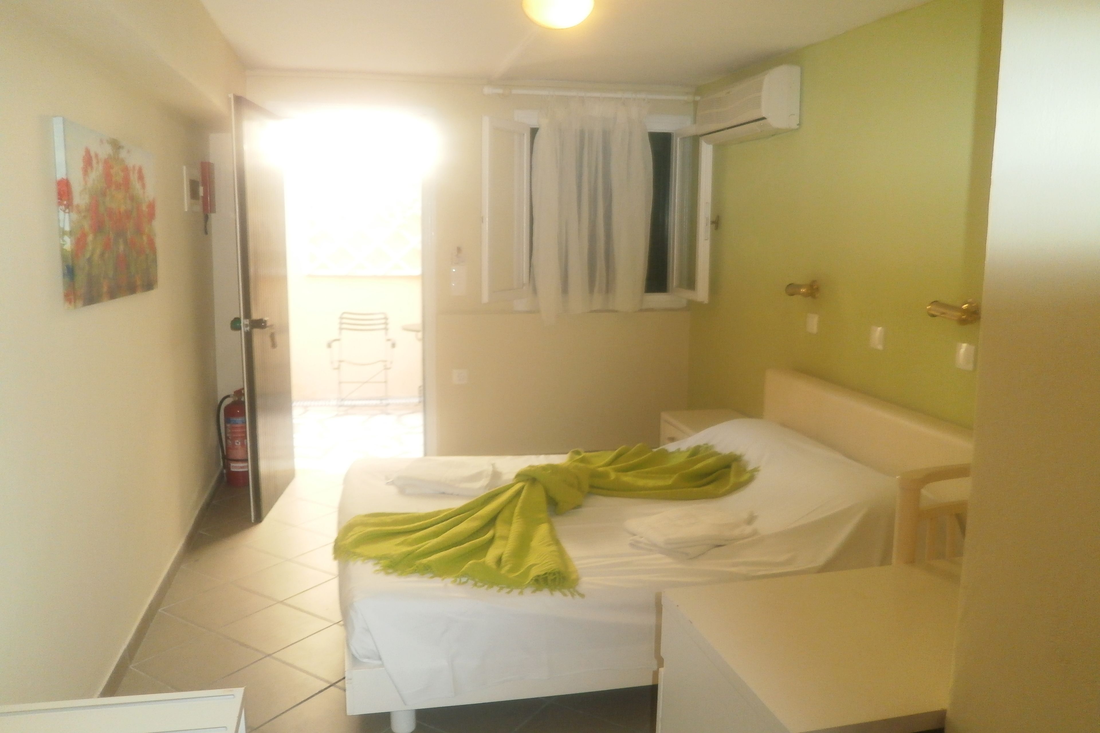 A small, clean room with a bed, a chair, a painting on the wall, and a window with curtains.
