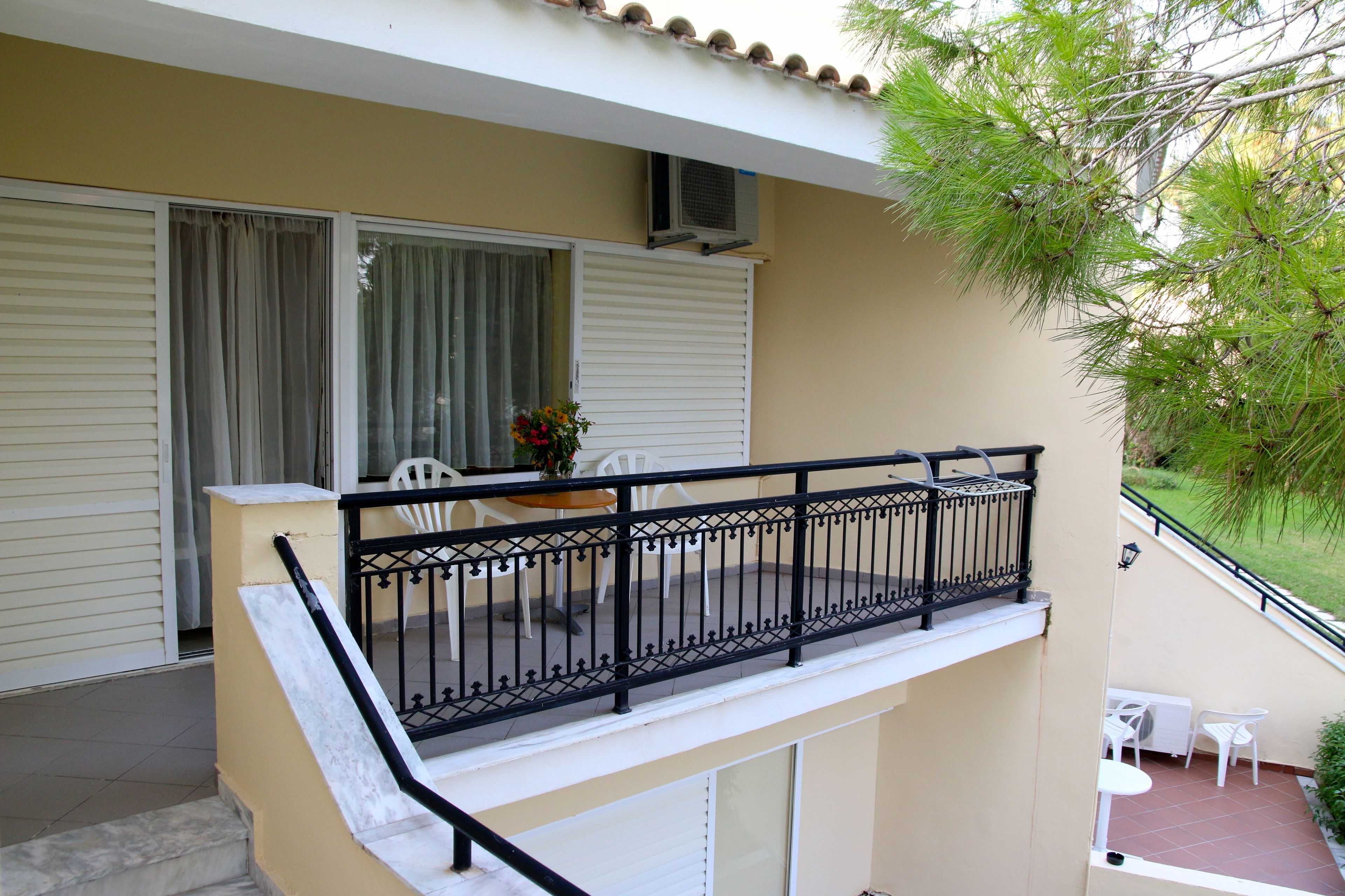 Un balcone con ringhiera in metallo nero, un tavolo e sedie bianche e un vaso con fiori.