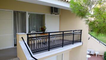 Un balcone con ringhiera in metallo nero, un tavolo e sedie bianche e un vaso con fiori.