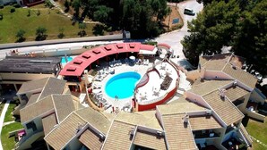 Una piscina circular rodeada por una terraza techada con varias zonas de descanso y un tobogán acuático central.
