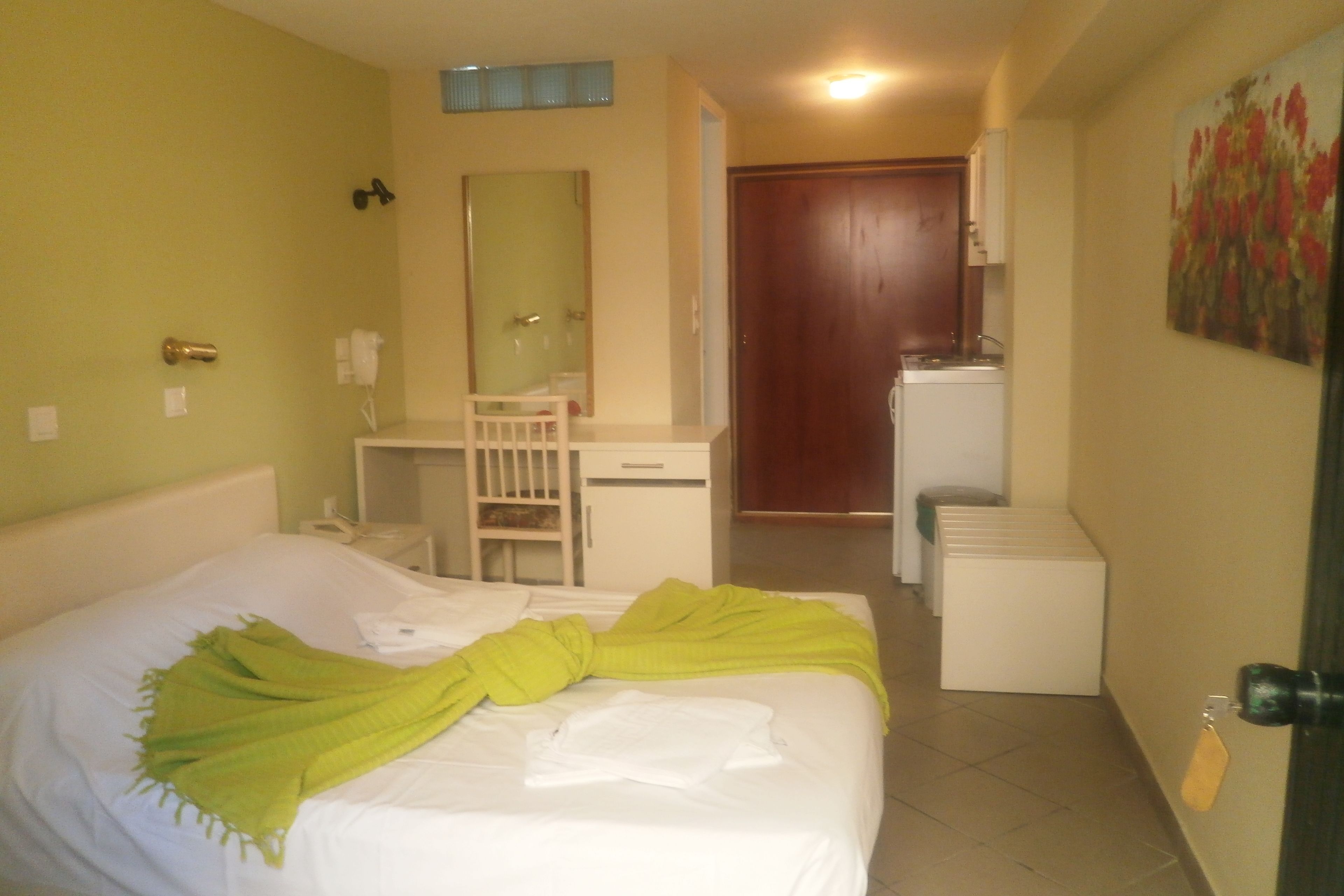 A hotel room with a bed, a desk, a chair, a mirror, and a door.