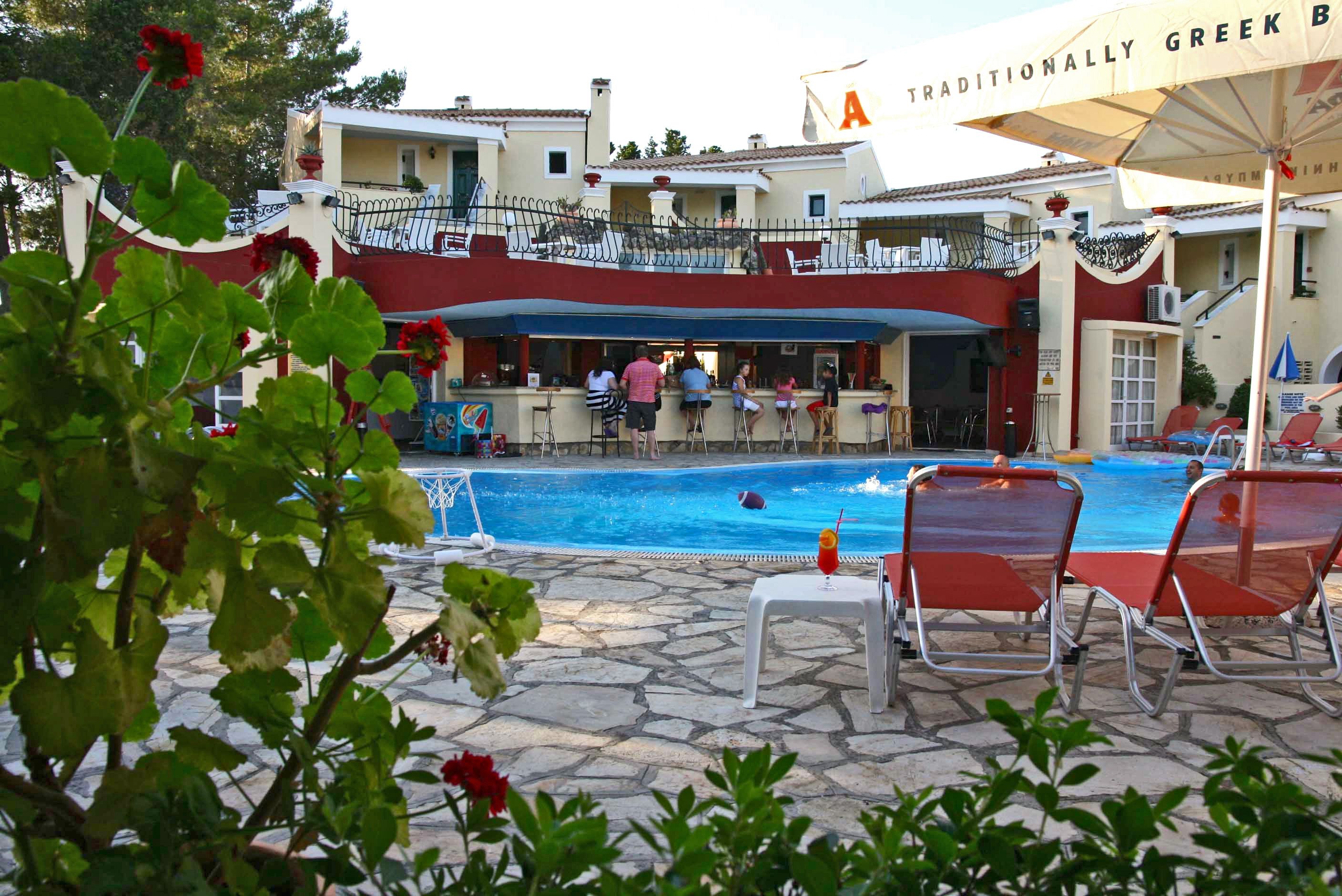 Un área junto a la piscina con un bar, sillones de descanso y un edificio con balcones.