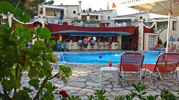 Un área junto a la piscina con un bar, sillones de descanso y un edificio con balcones.