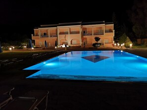 A swimming pool with a geometric tile pattern, surrounded by lounge chairs and umbrellas, with a building in the background.