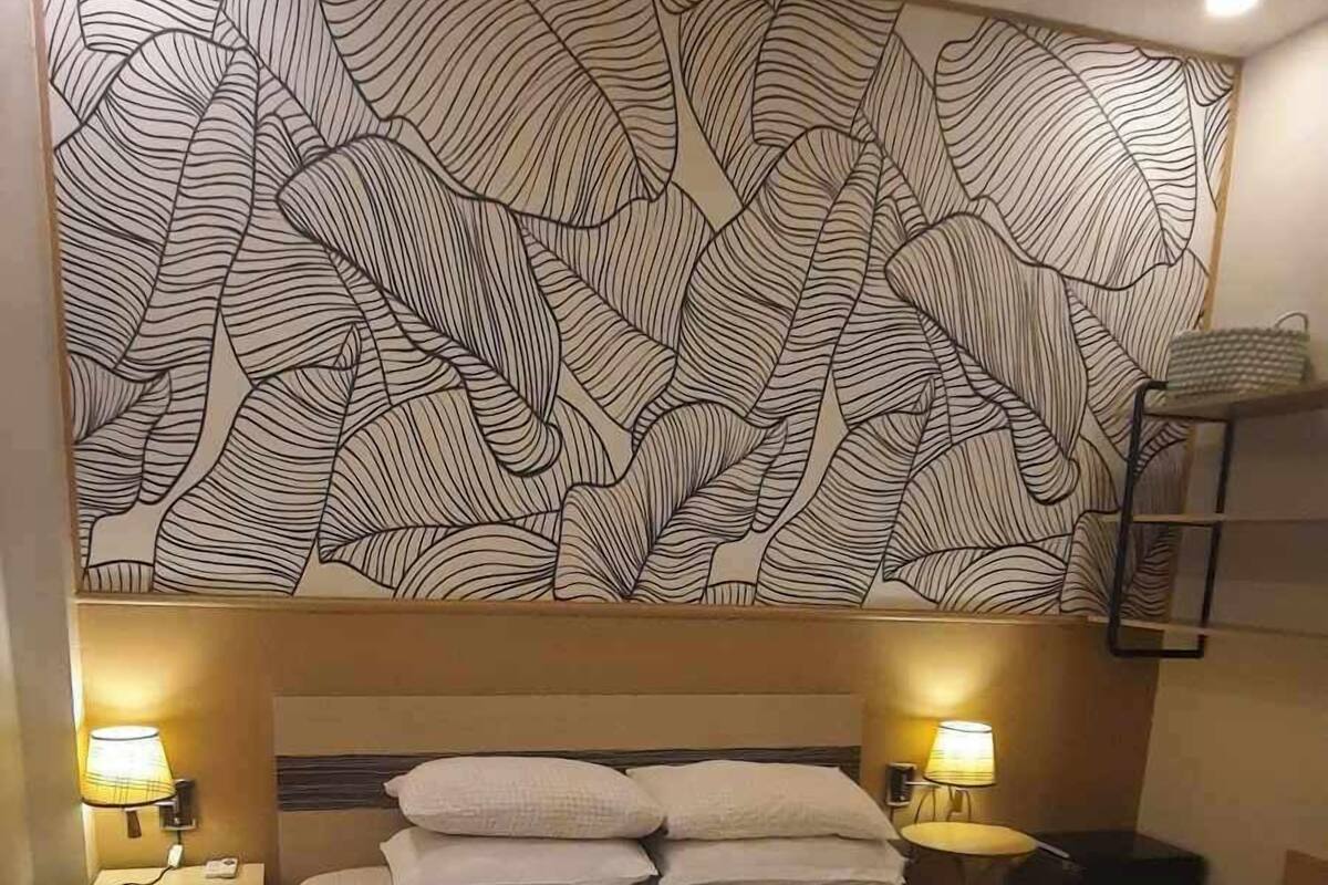 Een hotelkamer met een groot bed, twee nachtkastjes met lampen, een behang met patroon en een plafondlamp.
