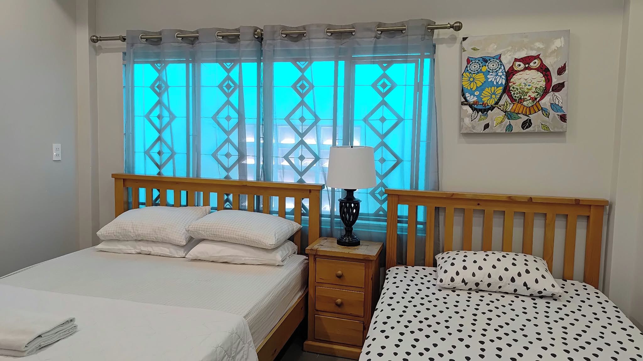Un dormitorio con cama, mesita de noche, lámpara y ventana con cortinas estampadas.