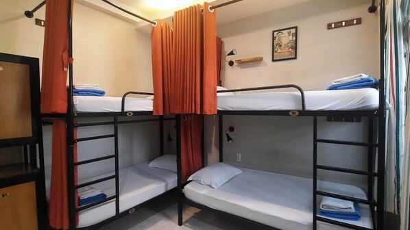 Habitación tipo dormitorio con literas, cortinas naranjas, un estante pequeño con una foto enmarcada y una lámpara de pared.