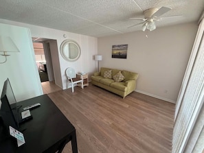 A living room with a sofa, a small table, a lamp, and a ceiling fan.