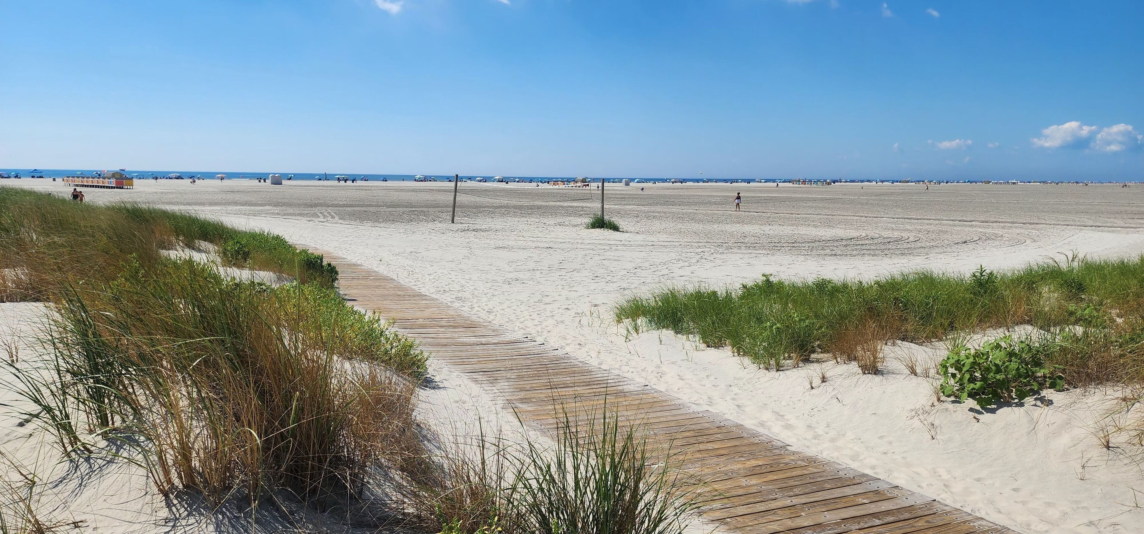 A sandy beach with a wooden boardwalk and sparse vegetation.