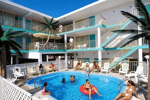 A multi-level hotel with a swimming pool, outdoor seating, and palm trees. - Sea Scape Inn (Wildwood Crest)