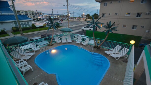 A swimming pool with lounge chairs and umbrellas, surrounded by a fence. - Sea Scape Inn (Wildwood Crest)