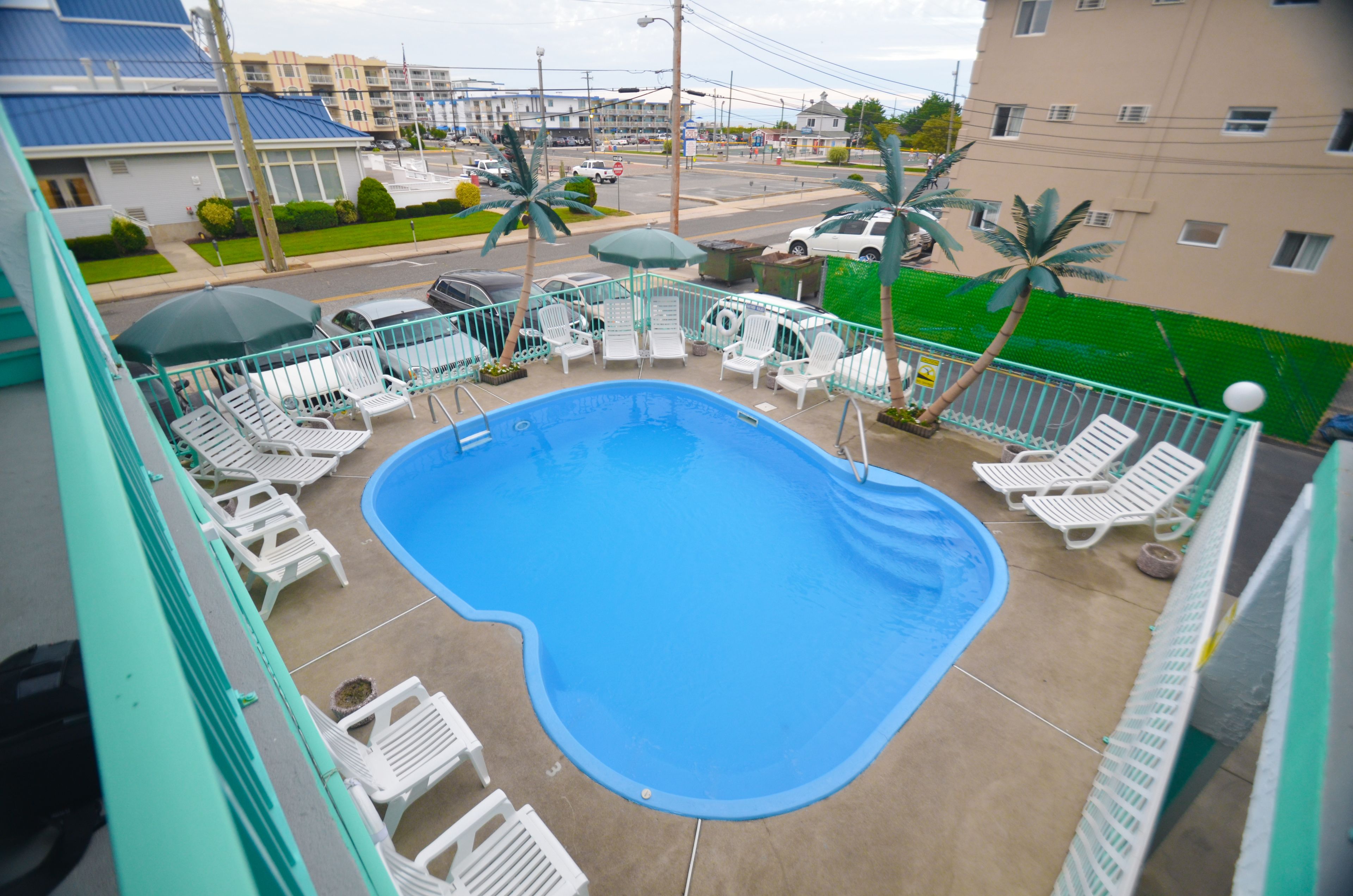A pool area with white lounge chairs and umbrellas, surrounded by a green fence.