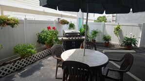 A patio with a round table, chairs, a grill, and potted plants. - Sea Scape Inn (Wildwood Crest)