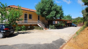 A building with a tiled roof, a covered outdoor area with a parking sign, and a gravel driveway.