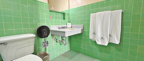 Une salle de bain avec des murs recouverts de carreaux verts, un lavabo blanc et deux serviettes blanches accrochées au mur.