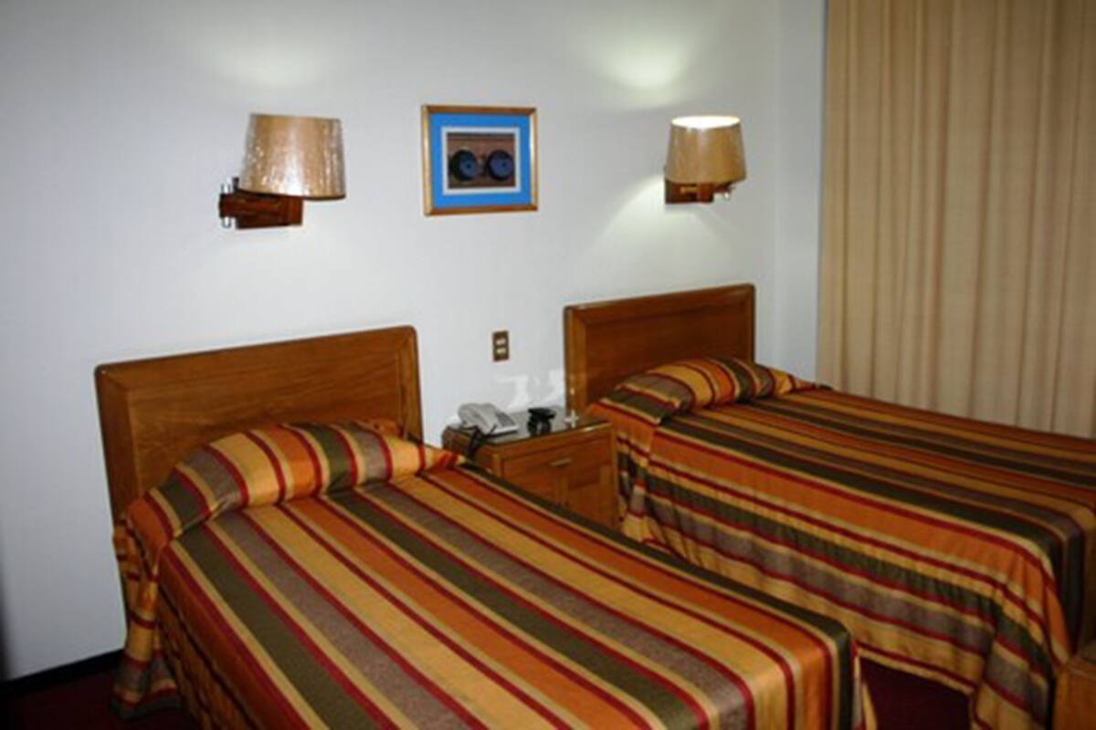 A hotel room with two beds, a nightstand, a lamp, and a framed picture on the wall.