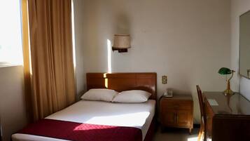 Une chambre d’hôtel équipée d’un lit, d’un bureau, d’une chaise, d’une lampe et d’un luminaire fixé au mur.