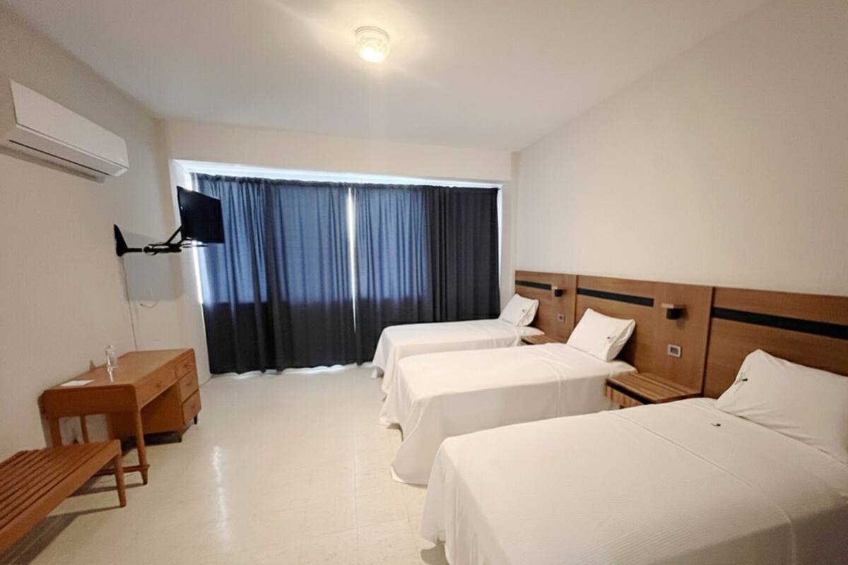 A hotel room with two single beds, a wooden desk, a TV, and a window with curtains.
