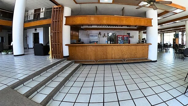 Un vestíbul ampli amb una recepció central, un ventilador de sostre i paviment de rajoles.