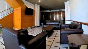 Un vestíbul espaiós amb un sostre alt, un ventilador de sostre, una televisió penjada a la paret i una zona de seients amb sofàs i una taula.