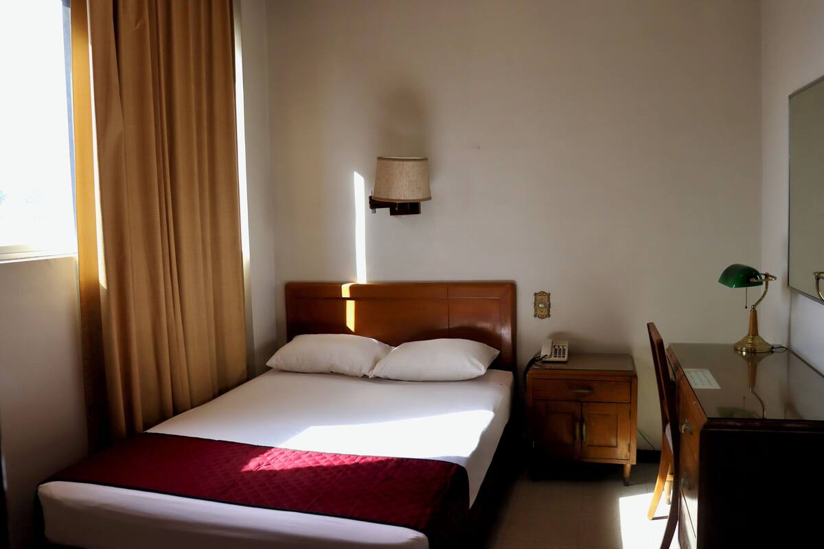 A hotel room with a bed, a nightstand, a desk, and a lamp.