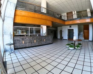 A spacious lobby with a marble reception desk, a staircase, and potted plants.